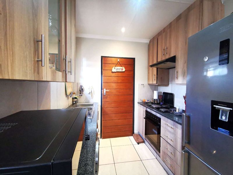 A functional galley-style kitchen featuring wood-finish cabinetry, granite countertops, built-in oven, hob, and extractor fan with tiled flooring.