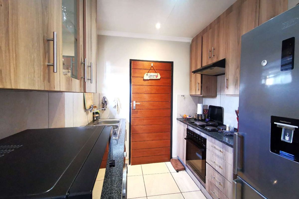 A functional galley-style kitchen featuring wood-finish cabinetry, granite countertops, built-in oven, hob, and extractor fan with tiled flooring.