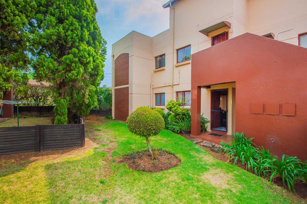A view of the apartment building exterior featuring a private garden area, landscaped lawn, and a covered entrance porch.