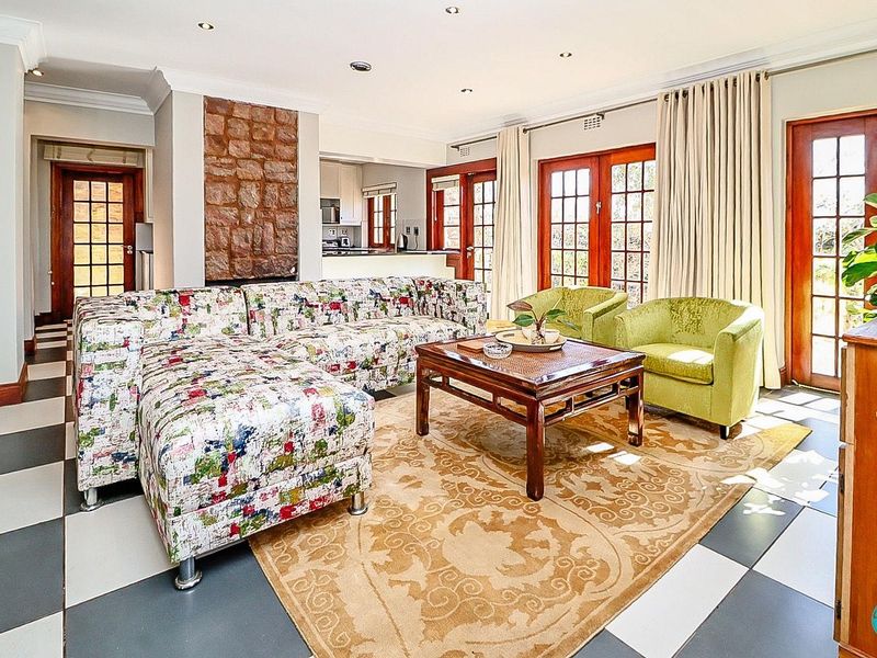 Spacious open-plan living area featuring a prominent stone fireplace, tiled flooring, and multiple timber-framed french doors providing access to the exterior.