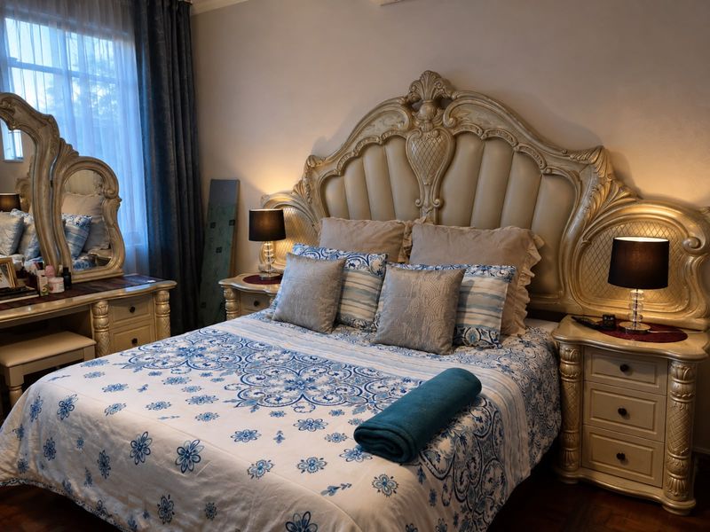 A well-maintained bedroom featuring classic ornate furniture, parquet flooring, and a large window with curtains, creating a comfortable and traditional living space.