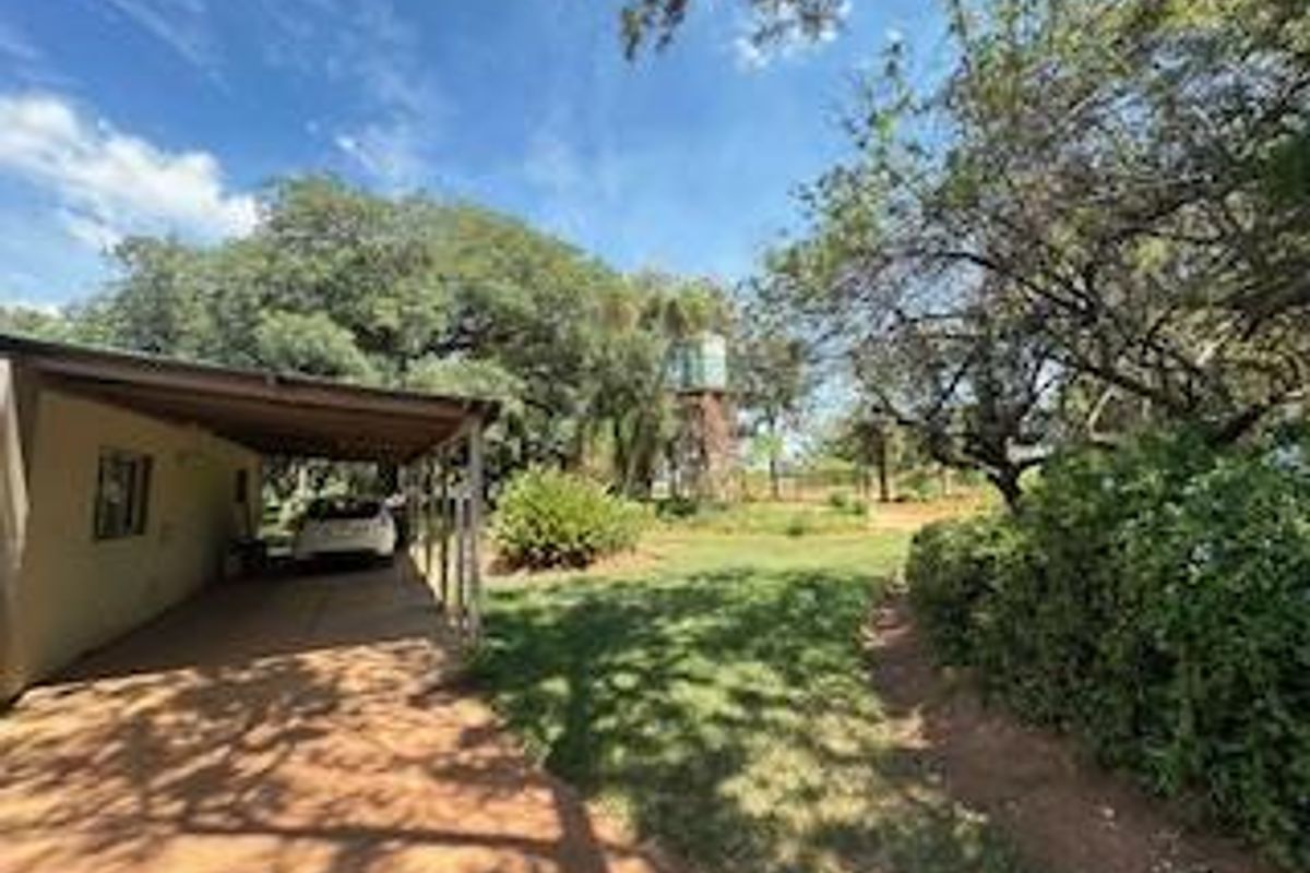 A spacious outdoor area featuring a covered carport, mature trees, and a water tank structure on a small holding property.