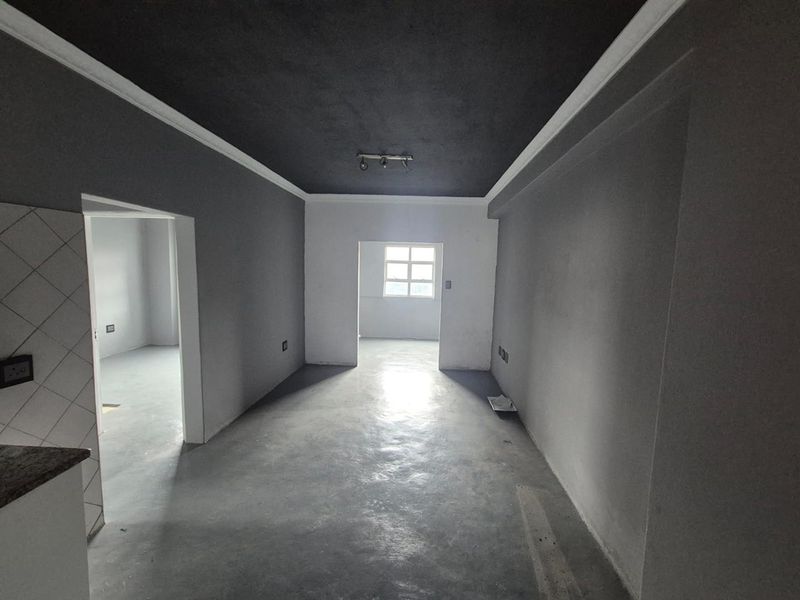 An empty open-plan living area featuring dark painted ceilings, neutral walls, and tiled flooring, offering a blank canvas for interior design.