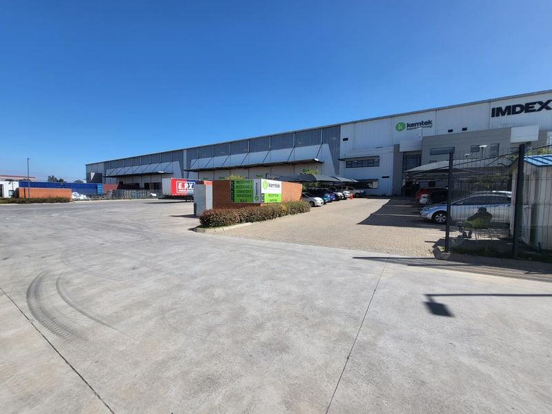 Wide-angle view of an industrial facility featuring a large concrete yard, paved parking area, and modern warehouse building with clear signage.