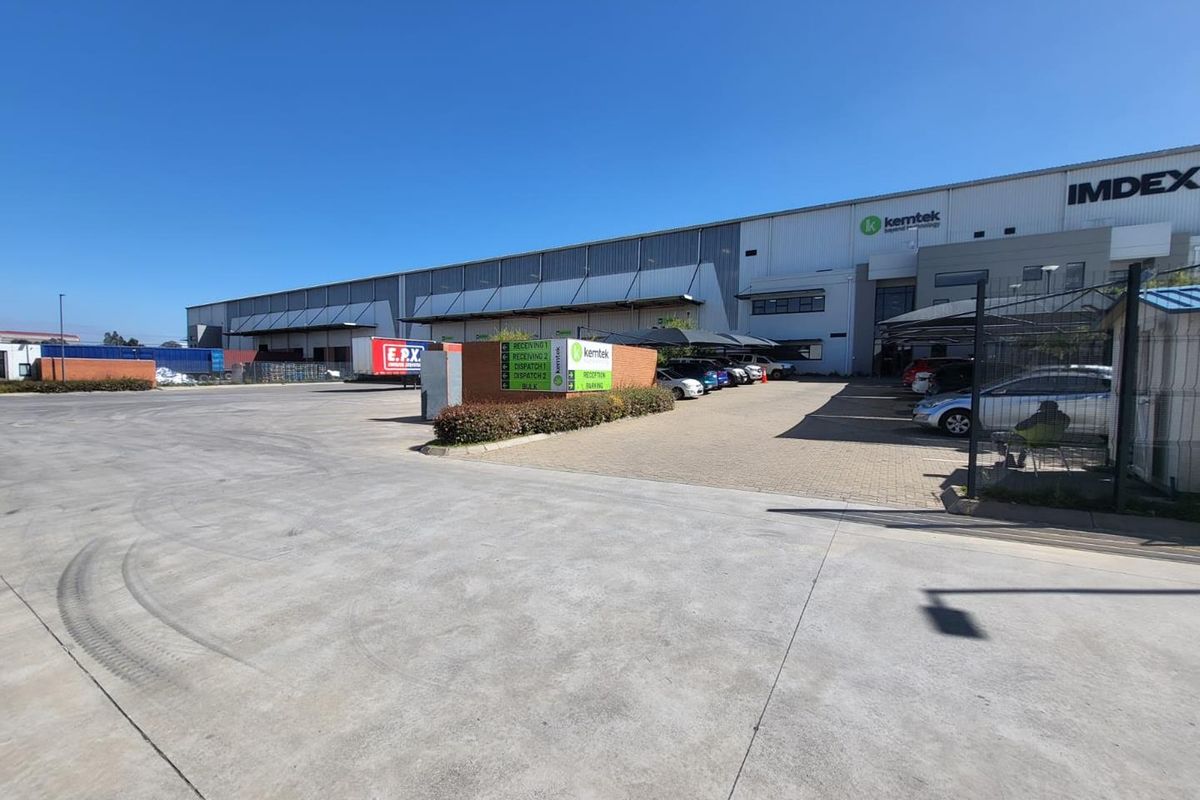 Wide-angle view of an industrial facility featuring a large concrete yard, paved parking area, and modern warehouse building with clear signage.