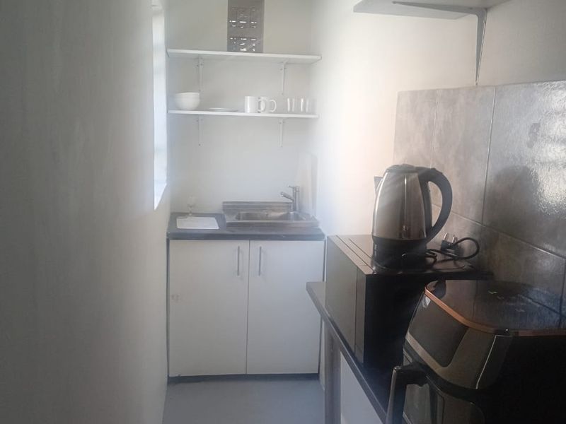A compact scullery or kitchenette area featuring built-in cabinetry, a stainless steel sink, tiled splashback, and open shelving for storage.