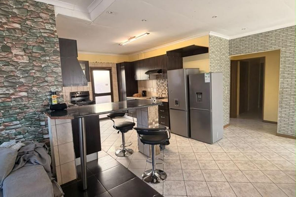 Open plan kitchen featuring dark cabinetry, breakfast bar, and tiled flooring, seamlessly connecting to the living area.
