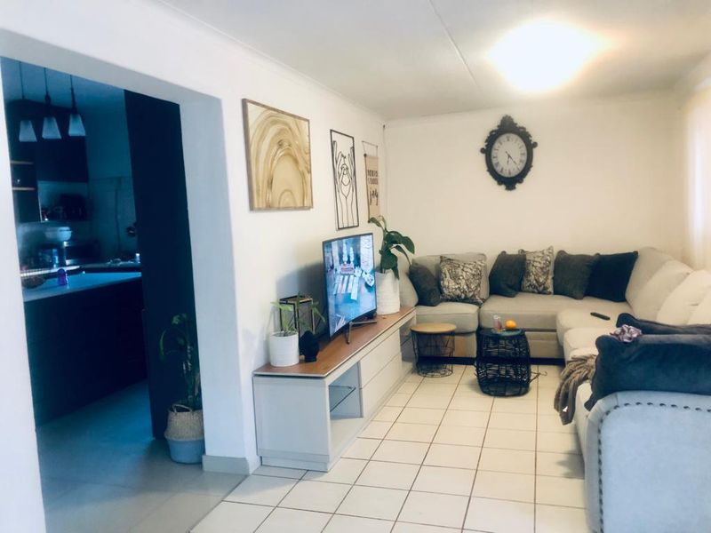A comfortable living room featuring ceramic floor tiles and a coved ceiling, with an open-plan layout connecting to the adjacent kitchen area.