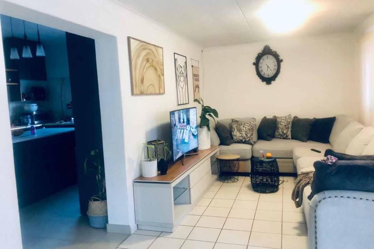 A comfortable living room featuring ceramic floor tiles and a coved ceiling, with an open-plan layout connecting to the adjacent kitchen area.