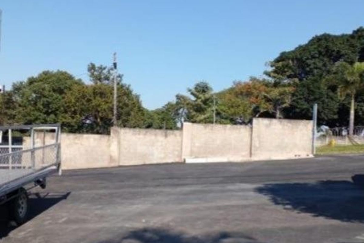 An outdoor paved area featuring a perimeter boundary wall and mature trees in the background.