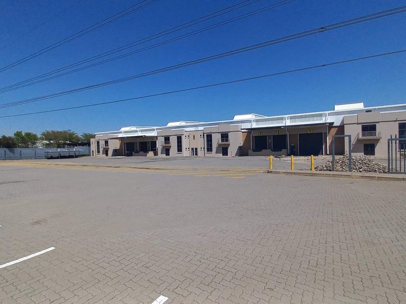 Wide-angle view of an industrial property featuring a large paved yard, multiple loading bays with roller shutter doors, and secure perimeter fencing.