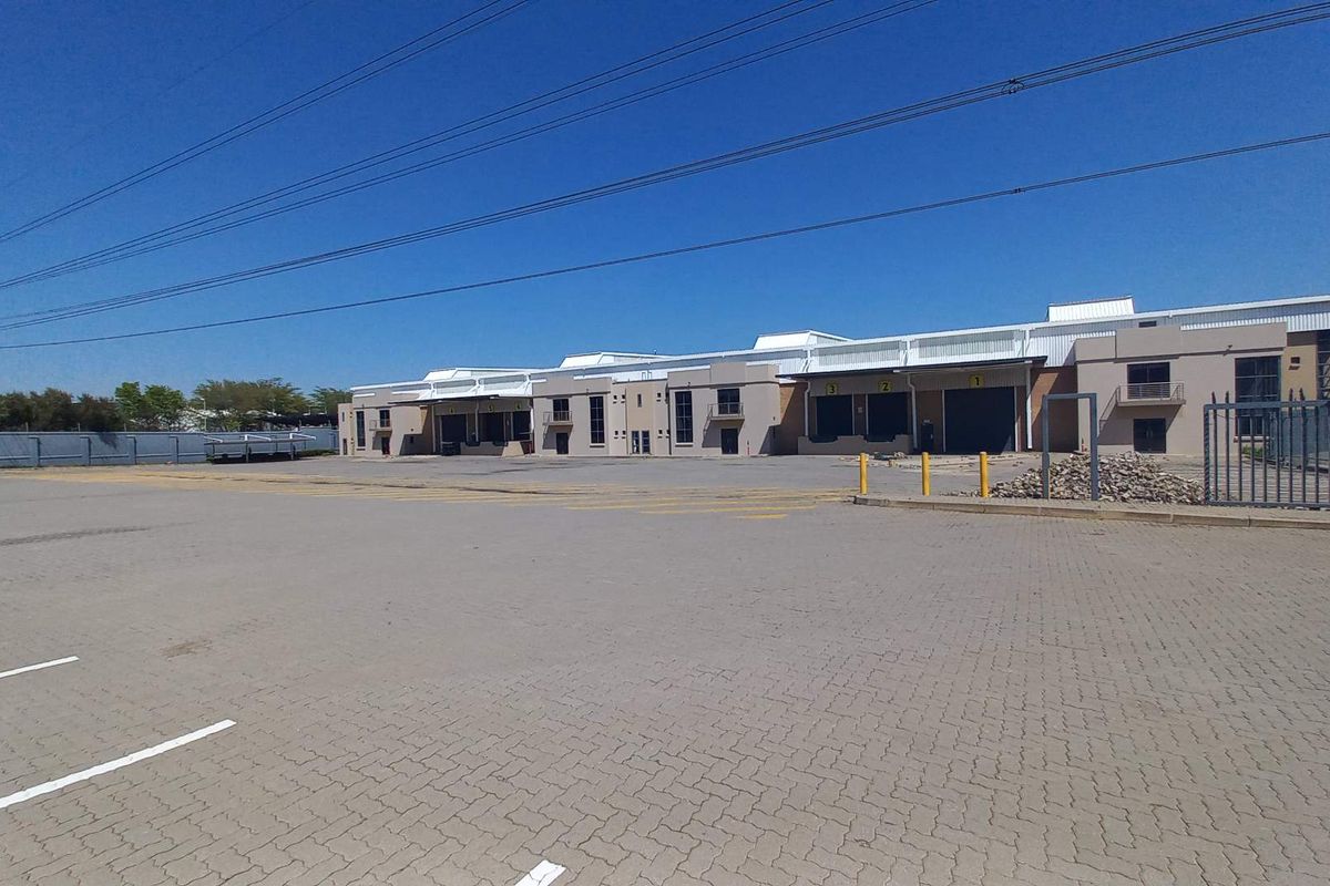 Wide-angle view of an industrial property featuring a large paved yard, multiple loading bays with roller shutter doors, and secure perimeter fencing.
