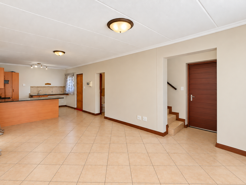 Spacious open-plan living and kitchen area featuring tiled flooring, neutral walls, and direct access to a staircase and internal rooms.