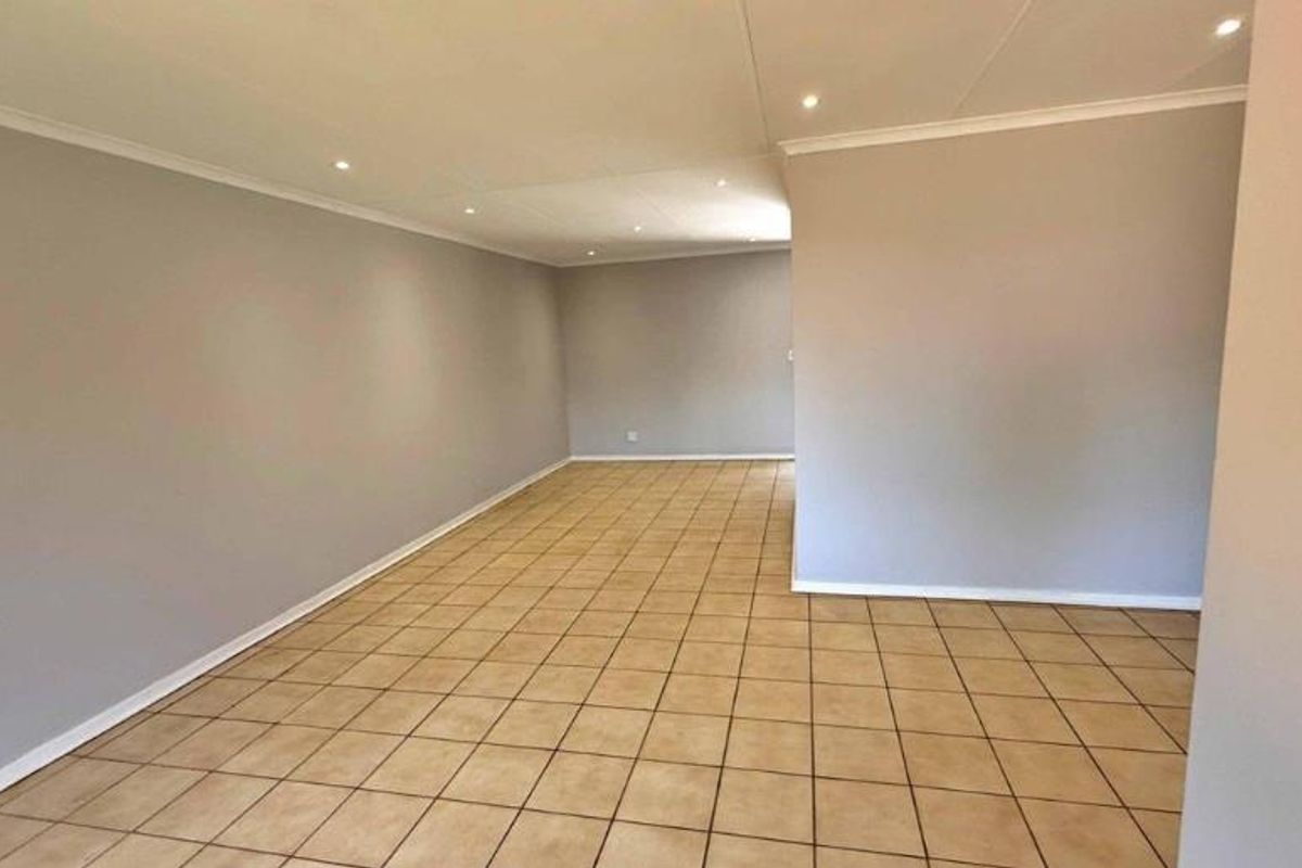 A spacious, empty living area featuring neutral wall tones, tiled flooring, and recessed ceiling downlights, offering a versatile blank canvas for interior design.