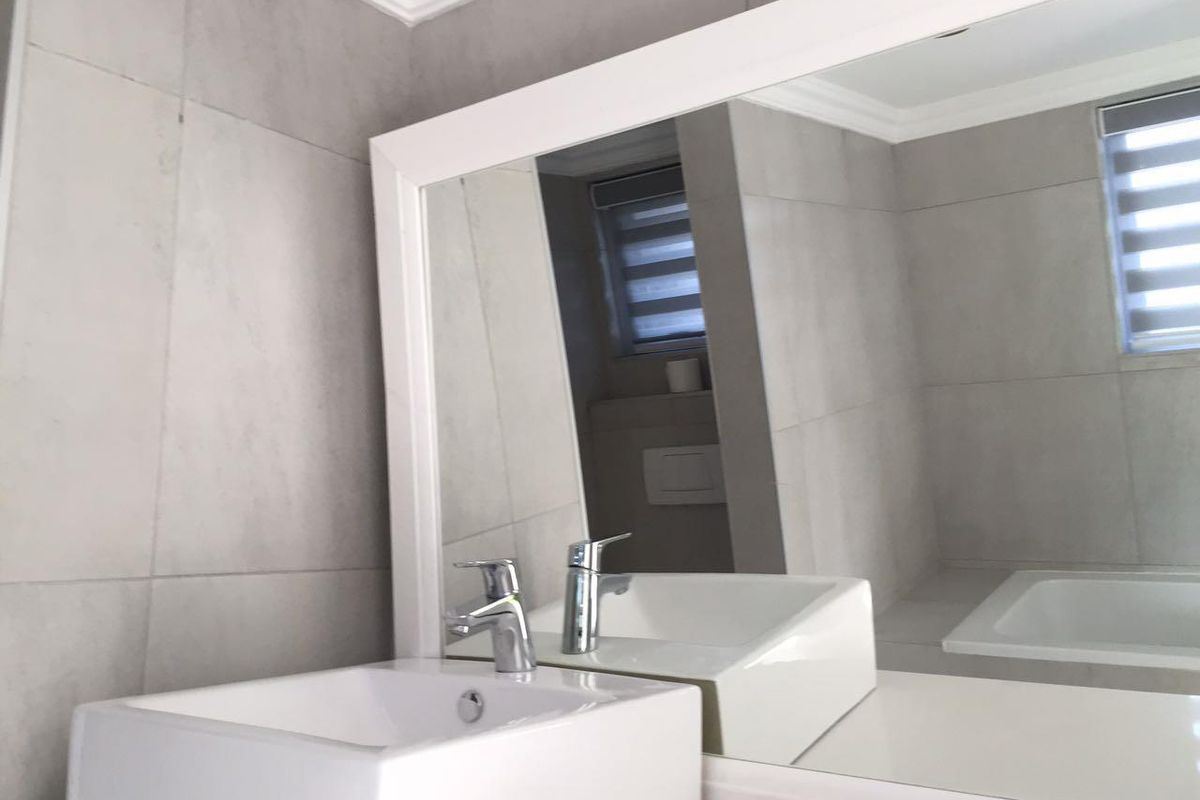 Modern bathroom featuring a sleek vessel sink, chrome faucet, large framed mirror, and neutral grey wall tiling.