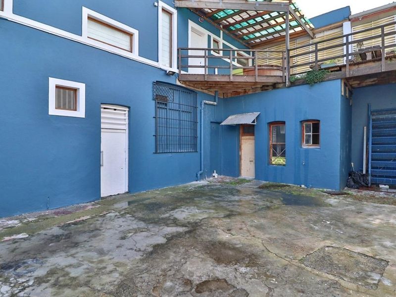 Rear courtyard area featuring a concrete surface, raised wooden deck, and external metal staircase, showing significant signs of wear and weathering.
