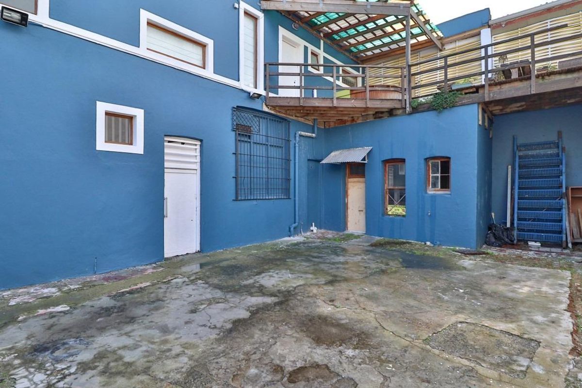 Rear courtyard area featuring a concrete surface, raised wooden deck, and external metal staircase, showing significant signs of wear and weathering.