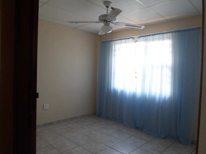 A vacant bedroom featuring tiled flooring, a ceiling fan, and a drop ceiling, offering a neutral canvas for personalization.