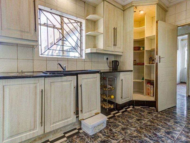 A functional kitchen featuring built-in cabinetry, a double sink, tiled backsplash, and a dedicated pantry cupboard with tiled flooring throughout.