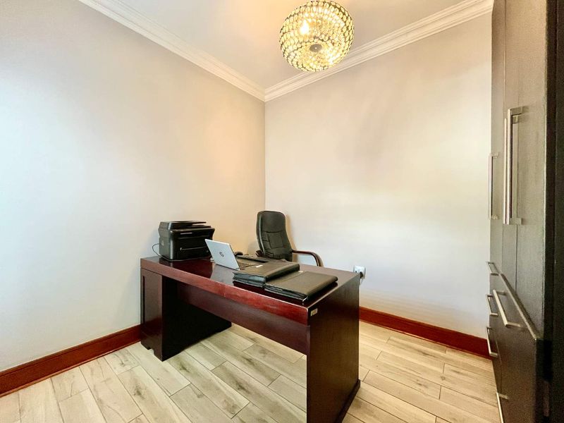 A well-maintained home office featuring wood-look tile flooring, crown molding, and built-in cabinetry, providing a functional and professional workspace.