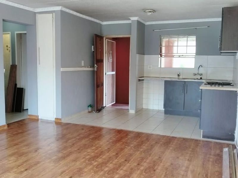 Open-plan living area featuring laminate flooring, a tiled kitchen zone with built-in cabinetry, hob, and sink, leading to a separate entrance.