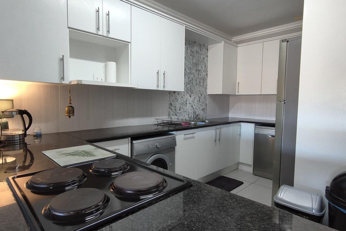 A functional kitchen featuring white cabinetry, dark granite countertops, a built-in electric hob, and tiled flooring.