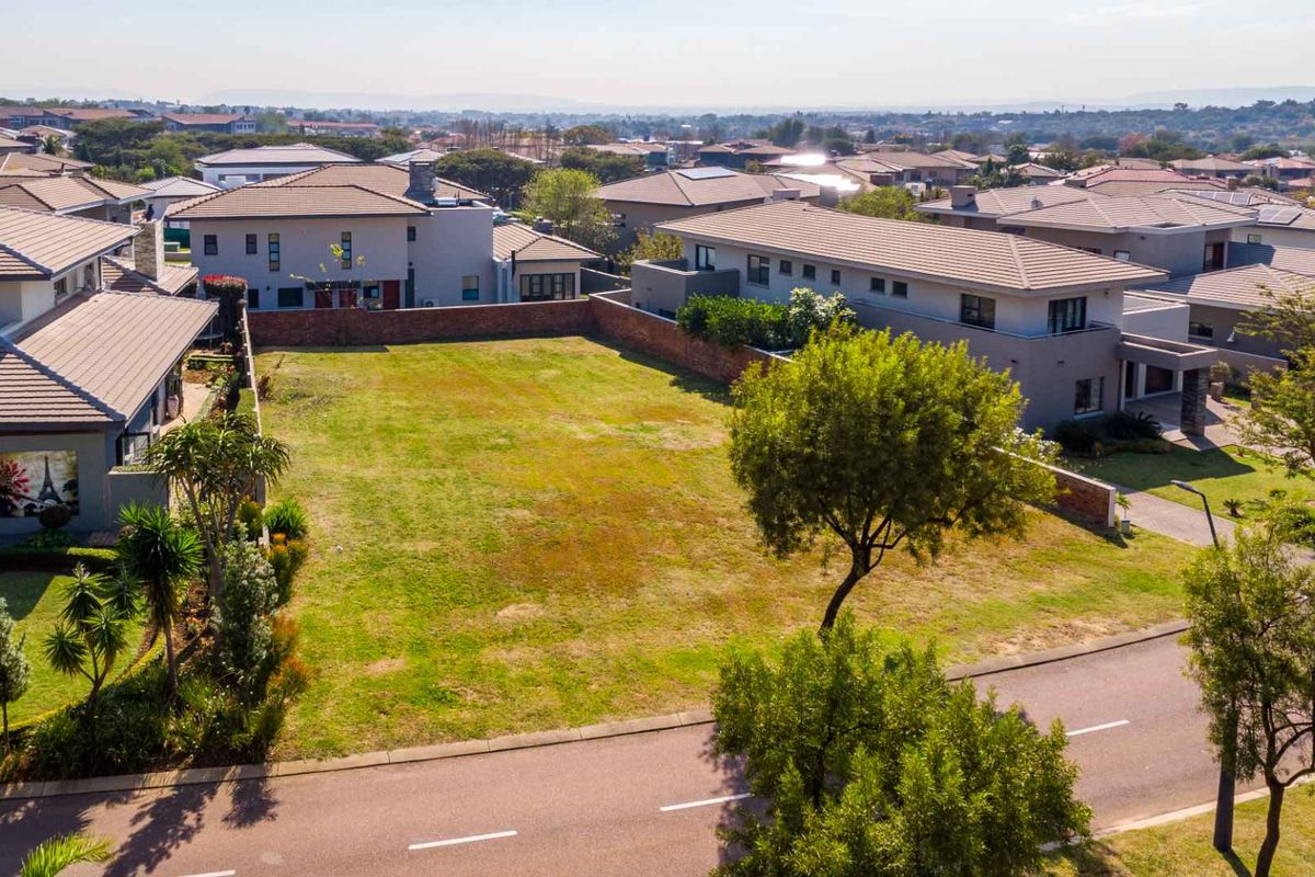 An elevated aerial view of a vacant residential plot situated within a developed estate, surrounded by established modern homes and paved street access.