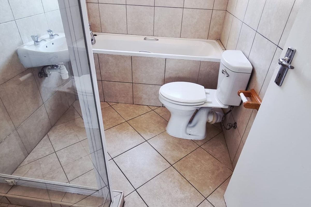 A functional bathroom featuring a shower enclosure, bathtub, toilet, and wall-mounted basin with neutral ceramic tiling throughout.