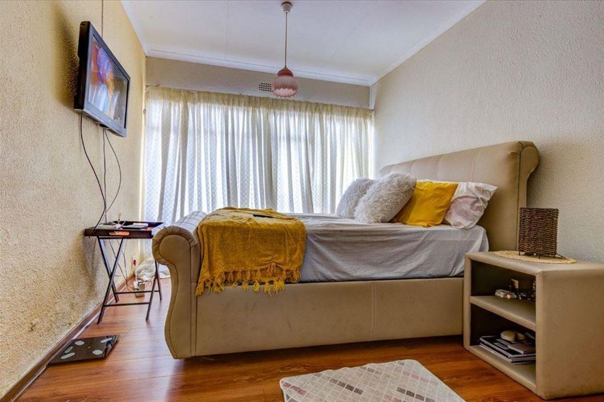 A bedroom featuring laminate flooring, textured walls, and a large window with curtains, providing a functional and comfortable living space.