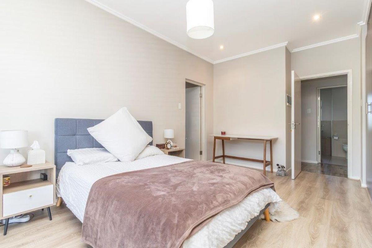 A well-maintained bedroom featuring light wood-look flooring, neutral wall tones, and an en-suite bathroom entrance.