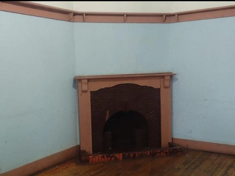 An empty living room featuring a traditional fireplace, timber flooring, and original picture rails, requiring cosmetic updates to restore its character.