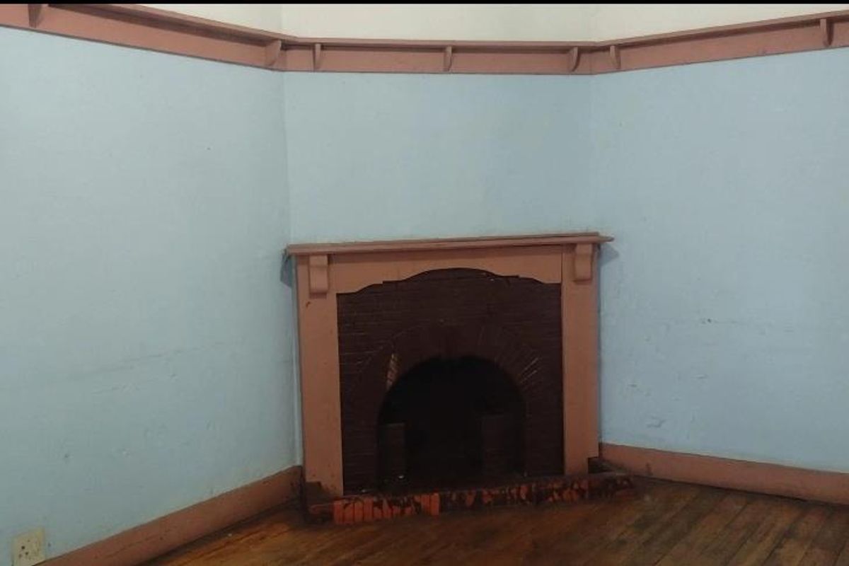 An empty living room featuring a traditional fireplace, timber flooring, and original picture rails, requiring cosmetic updates to restore its character.