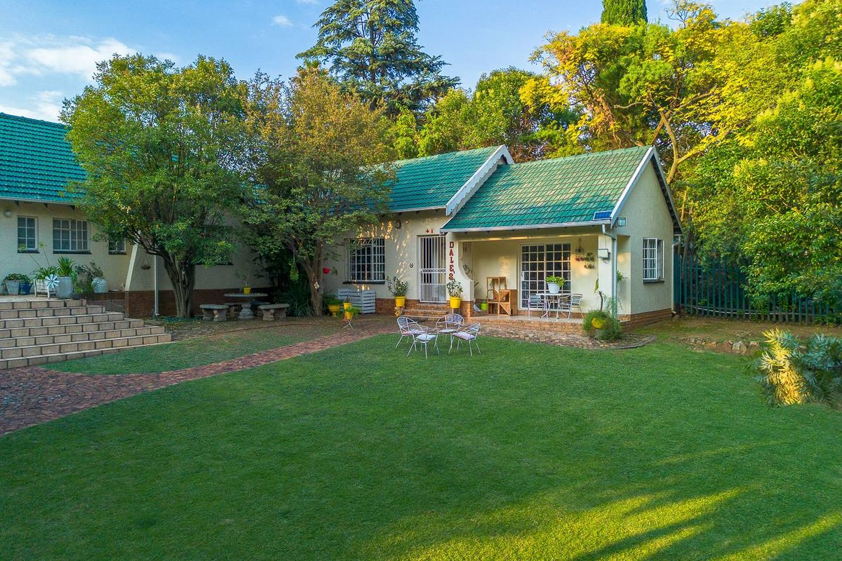 A well-maintained rear garden featuring a lush lawn, paved pathways, and a covered patio area attached to the main house structure.