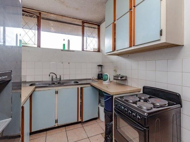 A dated kitchen featuring original cabinetry, tiled backsplash, and laminate countertops, offering significant potential for a modern renovation and aesthetic update.