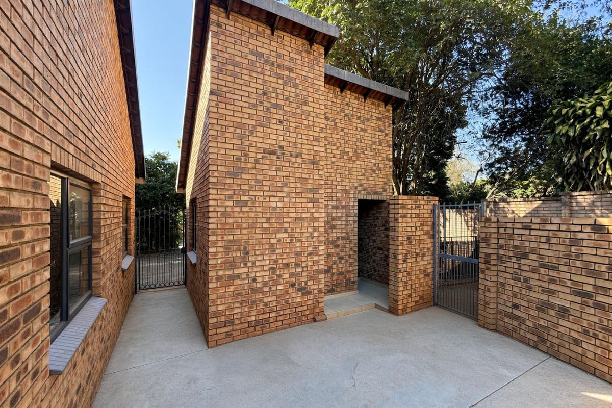 A side courtyard area featuring face brick walls, concrete paving, and secure metal gates providing access to the property exterior.