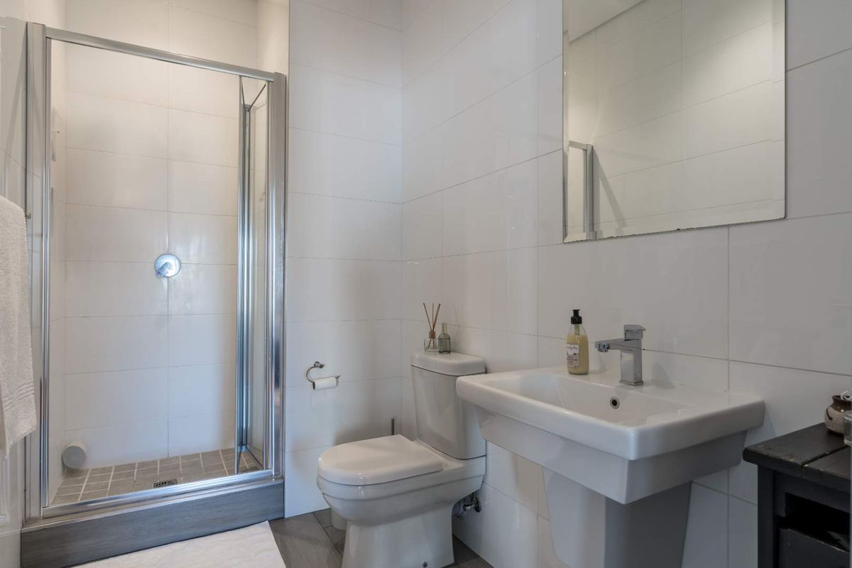 A clean, modern bathroom featuring a glass-enclosed shower, pedestal basin, and wall-mounted mirror with white tiled walls.