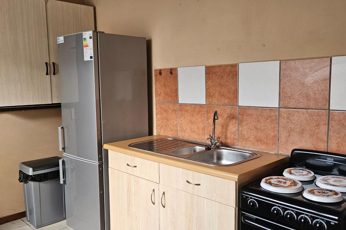 A functional kitchen area featuring light wood cabinetry, a stainless steel double sink, and a tiled splashback.