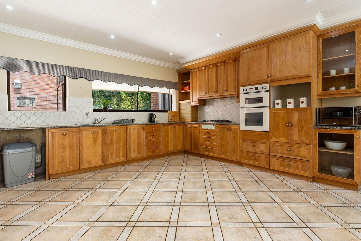 Spacious kitchen featuring extensive timber cabinetry, built-in double oven, gas hob, and tiled flooring with a large window overlooking the garden.