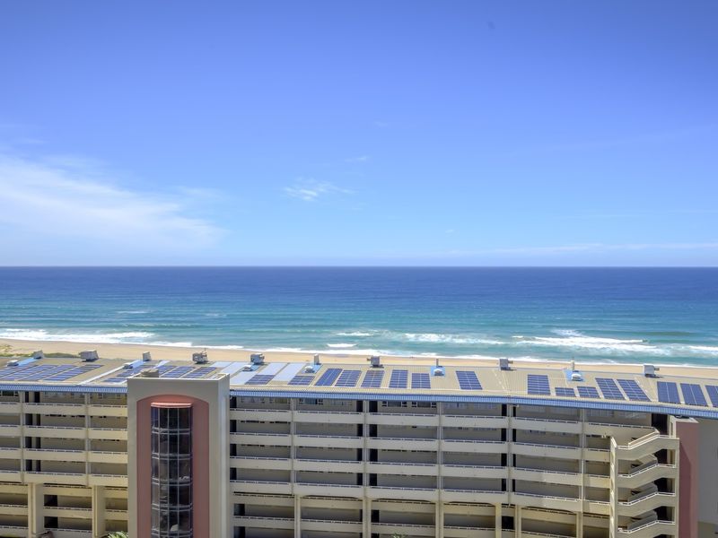 Aerial view of an apartment complex featuring rooftop solar panels and direct oceanfront proximity.