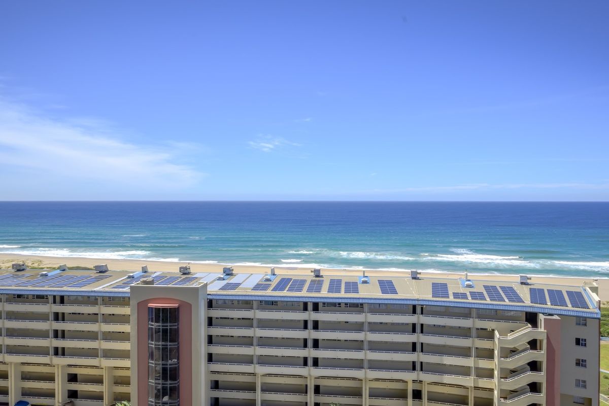 Aerial view of an apartment complex featuring rooftop solar panels and direct oceanfront proximity.