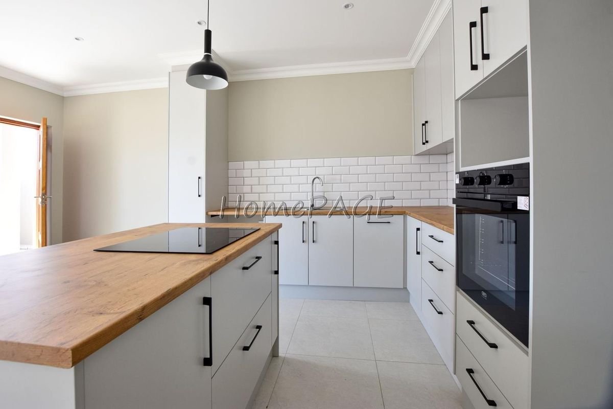 Modern kitchen featuring light grey cabinetry, wooden countertops, a central island with a built-in hob, and a subway tile backsplash.