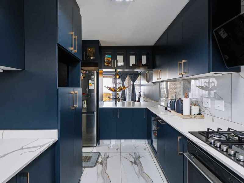 Modern galley-style kitchen featuring dark navy cabinetry, marble-look countertops and splashback, high-end gas hob, and polished porcelain floor tiles.