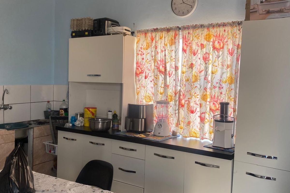 A functional kitchen area featuring white built-in cabinetry, dark laminate countertops, and a tiled splashback, providing essential storage and workspace.
