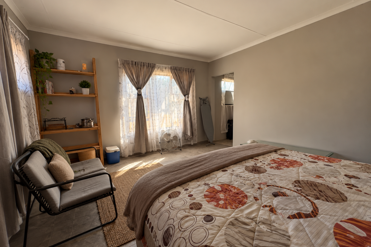 A well-lit bedroom featuring tiled flooring, neutral wall tones, and natural light through large windows with curtain treatments.