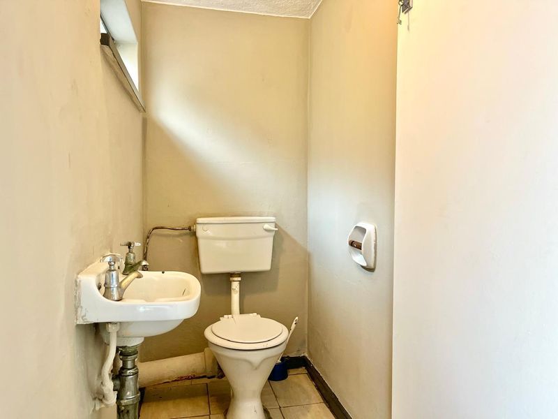 A compact guest bathroom featuring a wall-mounted basin and a standard close-coupled toilet with tiled flooring.