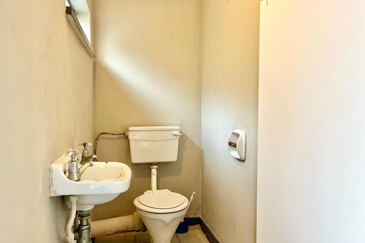 A compact guest bathroom featuring a wall-mounted basin and a standard close-coupled toilet with tiled flooring.