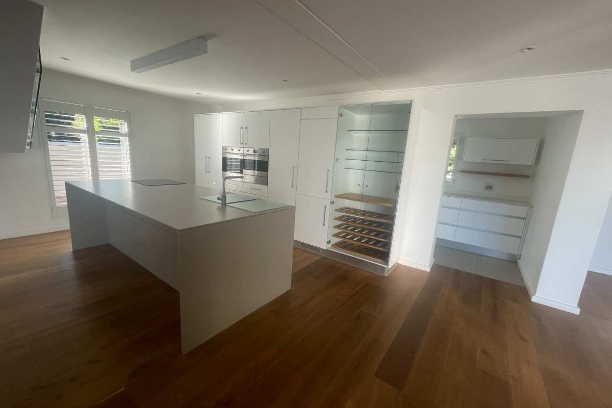 Modern kitchen featuring a large central island, integrated appliances, wine storage, and hardwood flooring, with an adjacent scullery area.