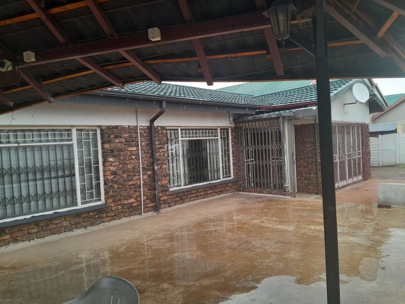 A covered outdoor patio area featuring exposed brick walls, security gates, and a tiled roof, providing a functional space for outdoor living.