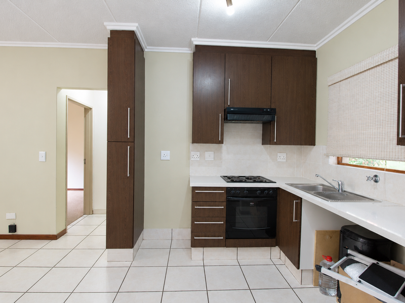 A functional kitchen featuring dark wood cabinetry, built-in oven and hob, tiled backsplash, and neutral tiled flooring.