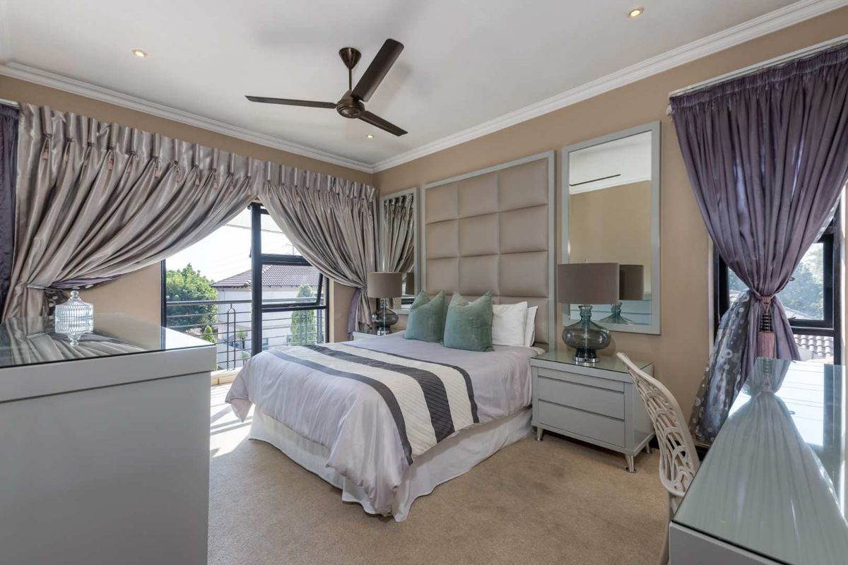 A well-maintained bedroom featuring a large upholstered headboard, recessed ceiling lighting, a modern ceiling fan, and access to a private balcony.